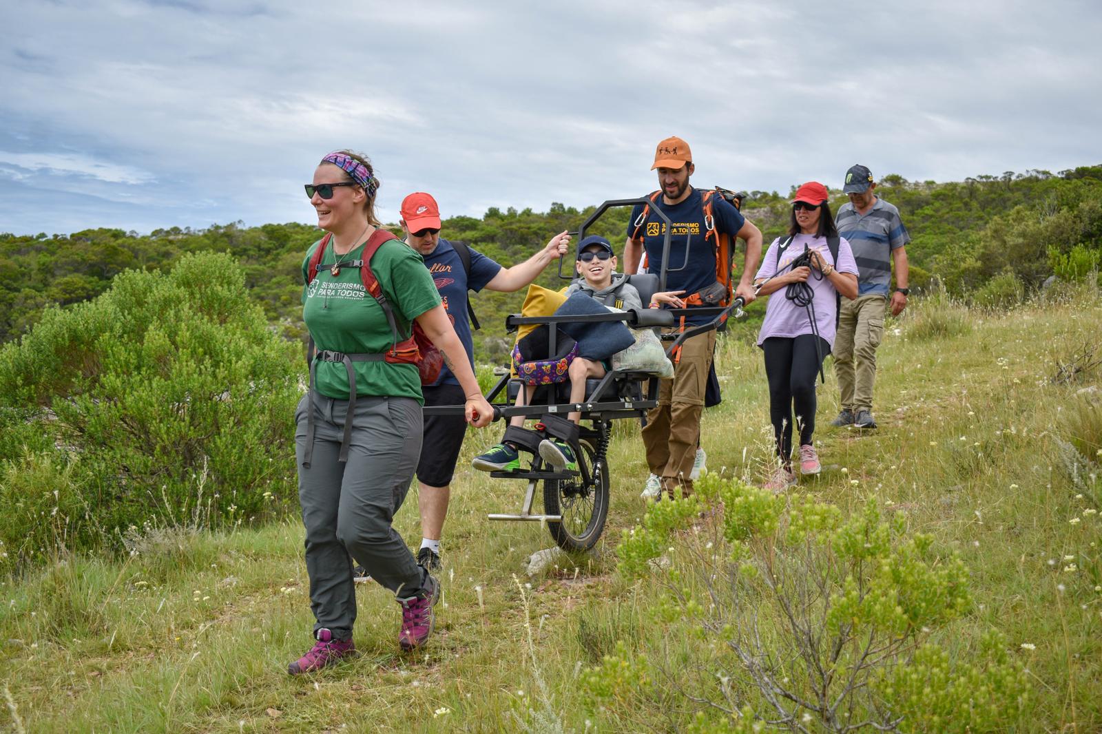 Personas practicando senderismo inclusivo con silla Joëlette en un sendero